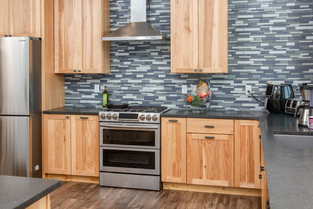 New modern kitchen with light wood cabinets, gray tile walls, and silver appliances
