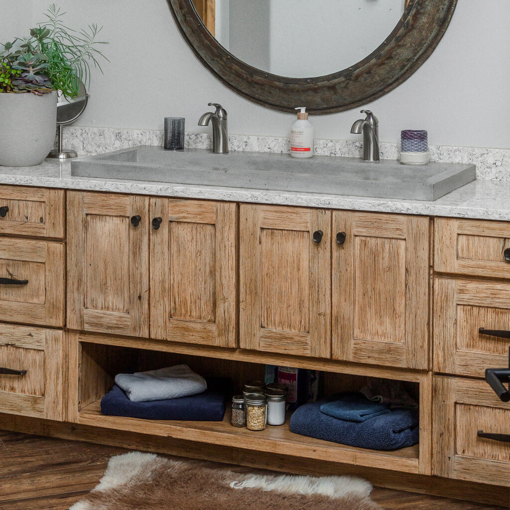 Bathroom with light wood cabinets, gray double sink with single round mirror on wall