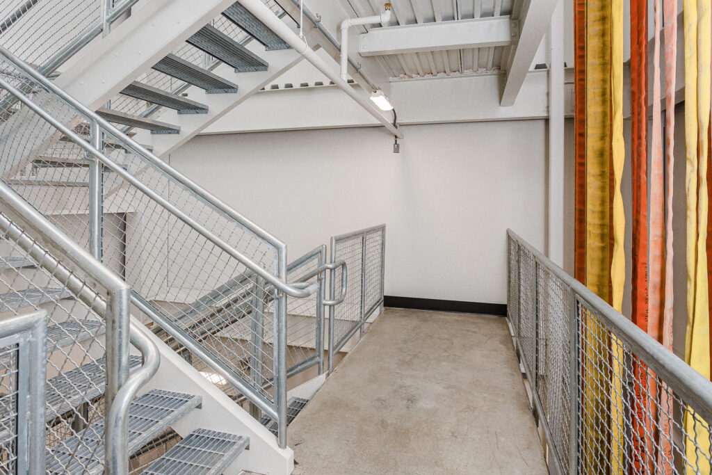 Metal stairs in a fire station with fire hoses hanging down on the side
