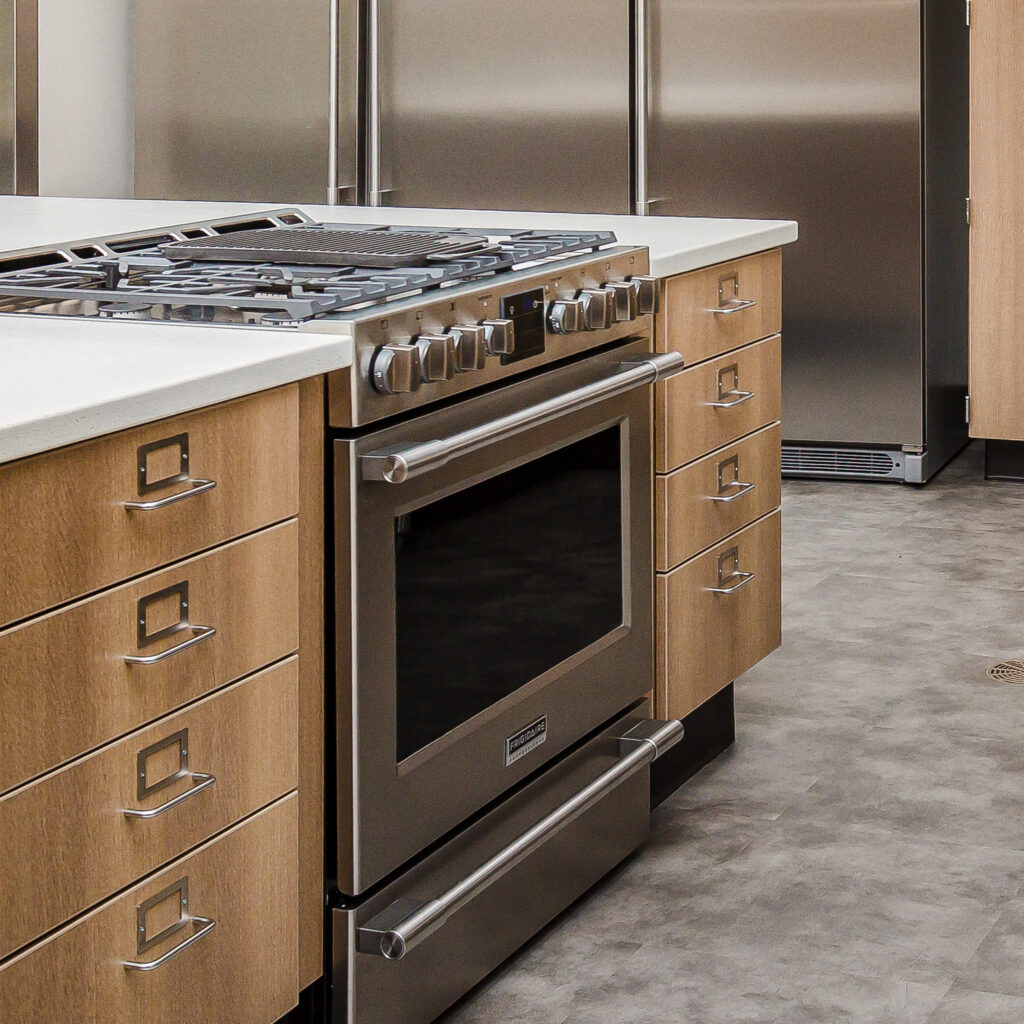 Large kitchen island with built-in silver oven and stove, white countertop, and tan drawers