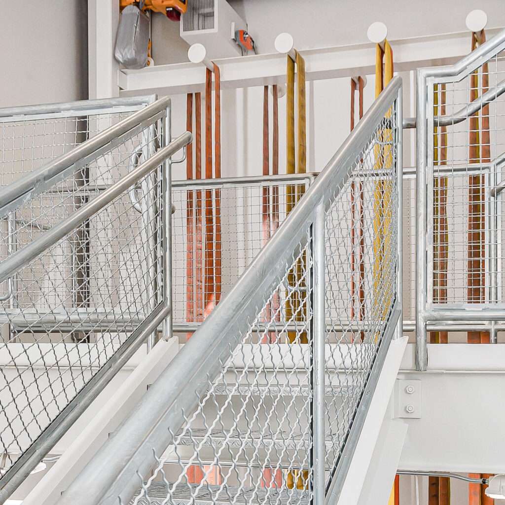 Metal stairs in a fire station with fire hoses hanging from metal support beam