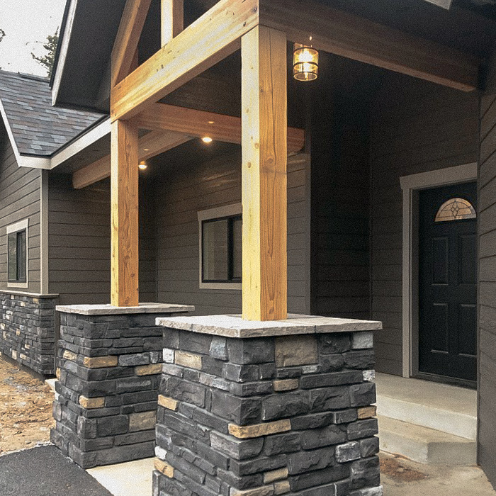 Front door of a new house with wooden beams on stone pillars holding up an overhang