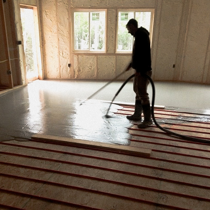 Worker pouring and smoothing concrete for the floor of a new building