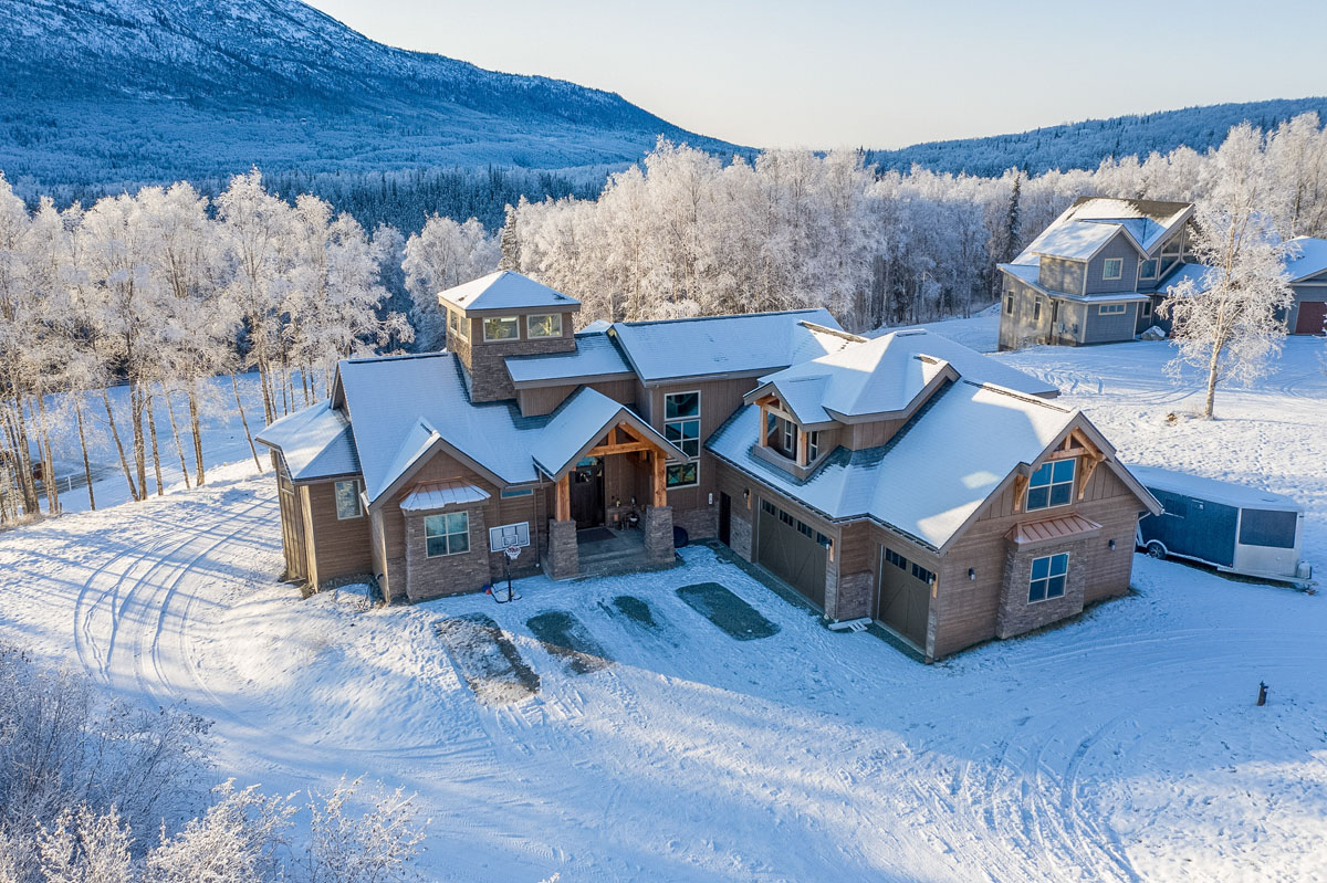 High-angle exterior of a large house in the snow with mountains in the background