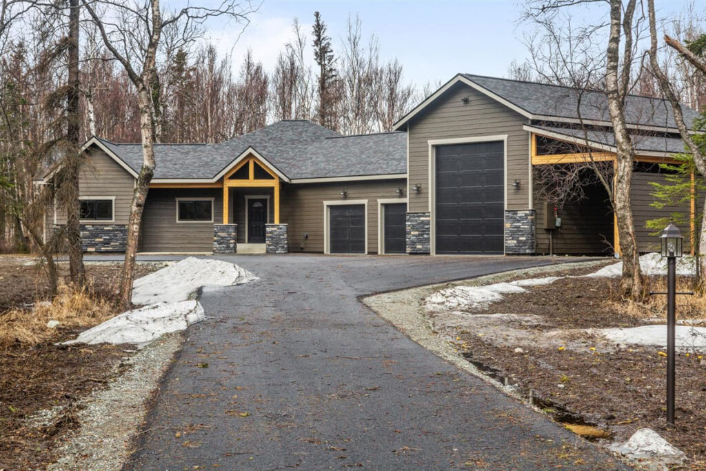 One-level home with light brown siding, three garage doors, and trees surrounding.