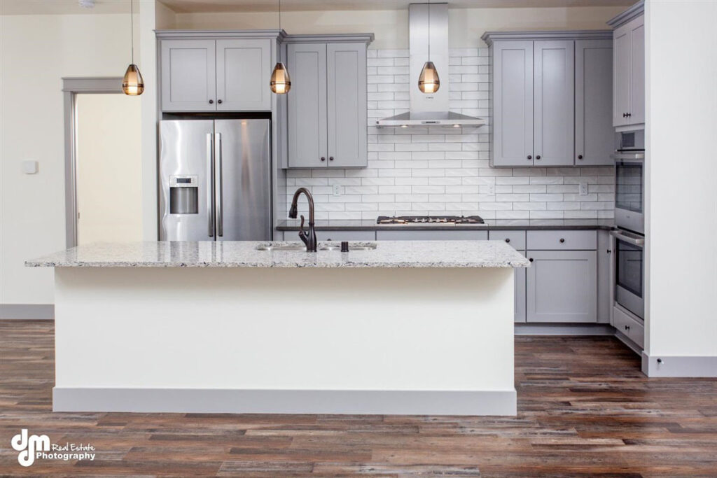 Remodeled kitchen with light gray cabinets, white island, stone countertops, white subway tile backsplash, and wood floors.