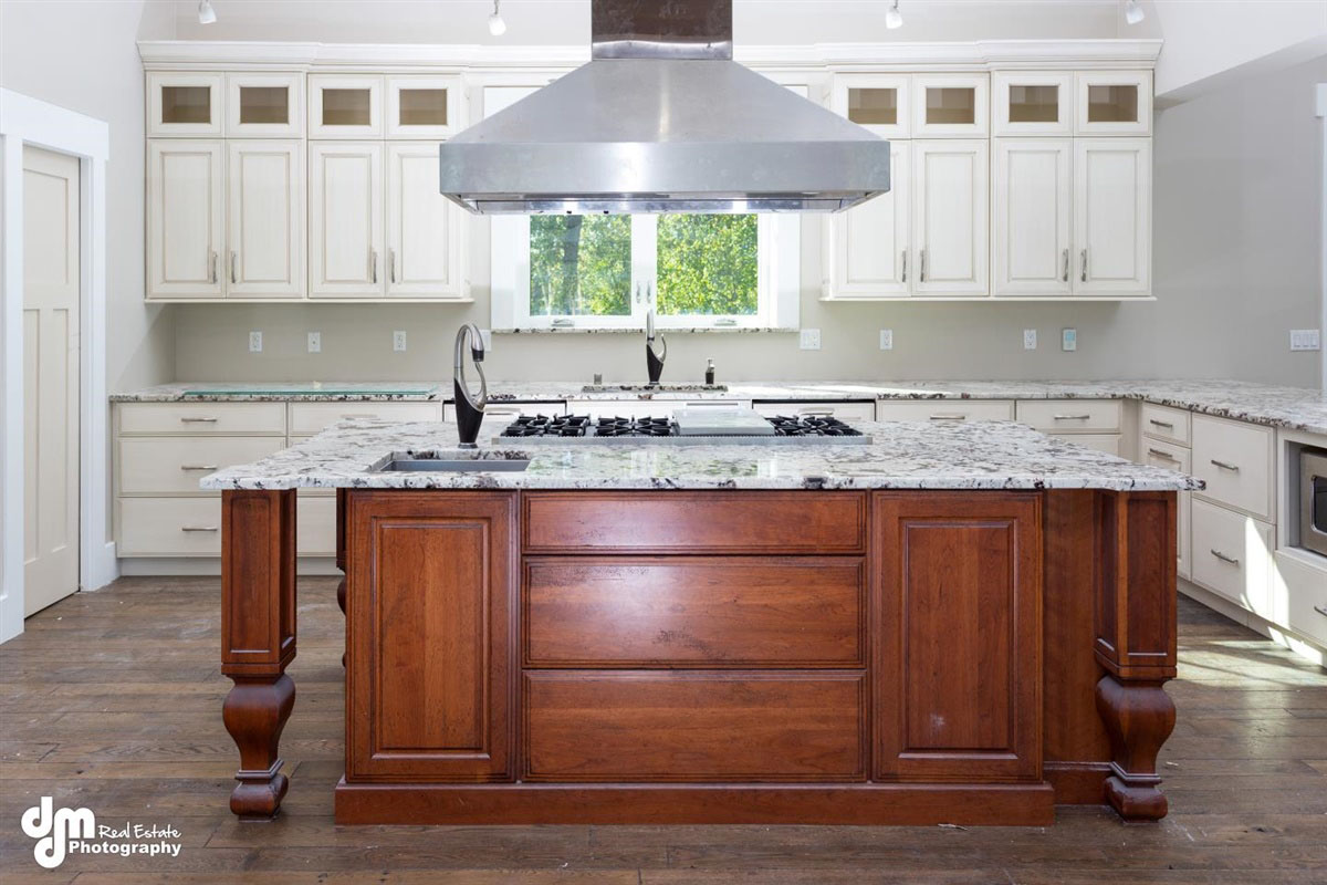 Large kitchen island with steel overhead extractor fan & white cabinets in background