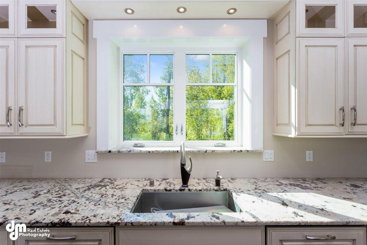 Newly installed kitchen sink in custom home underneath large kitchen windows with recess lighting