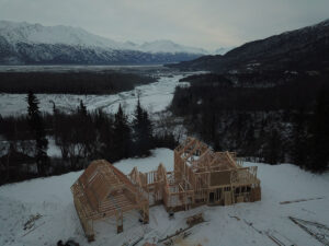 Framing of a house under construction on a snowy lot overlooking some woods