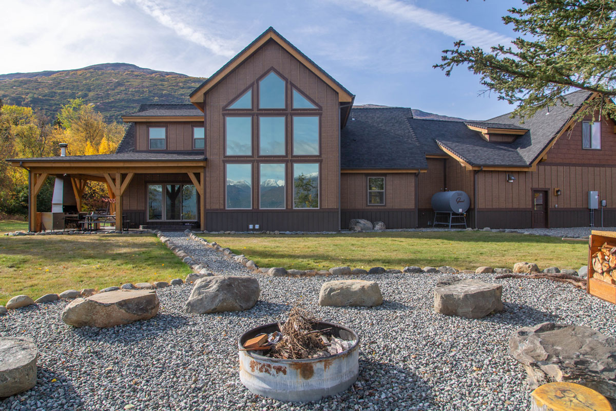Exterior of a large rural house with a large window wall facing mountains